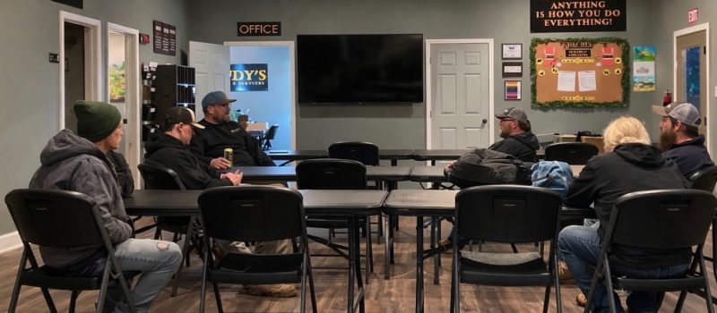 Lundy's Landscape Services staff members seated at tables in a conference room during a team meeting, with company signage and motivational poster reading "How You Do Anything Is How You Do Everything" visible on the walls
